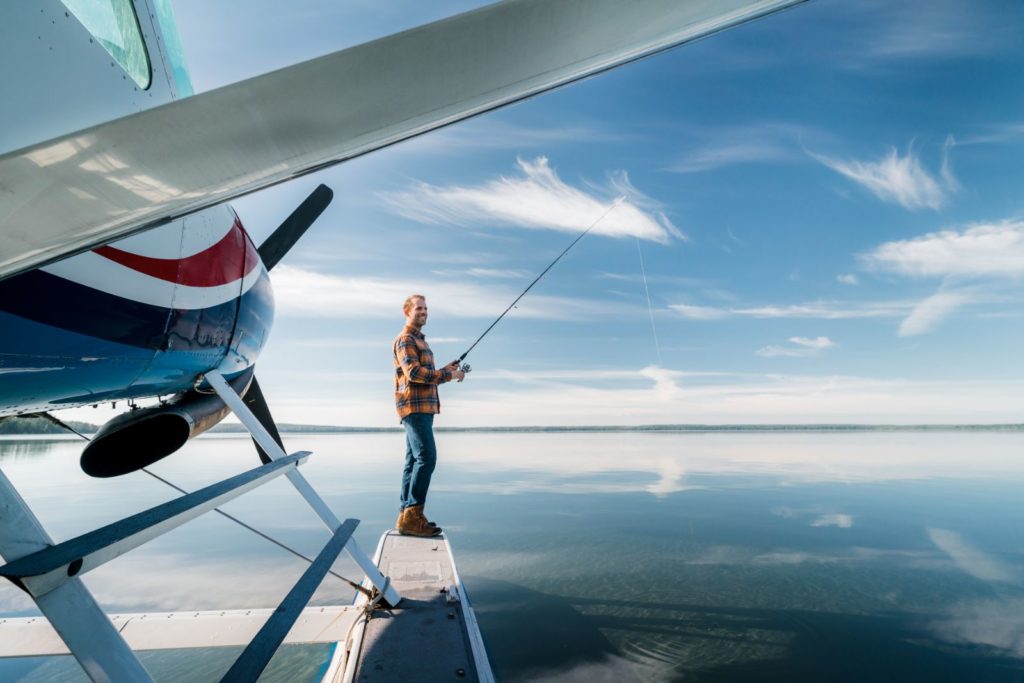 a man fishing off the doc of a a water plane at Lesser Slave Lake, with the plane in the foreground and the water and distant land in the background